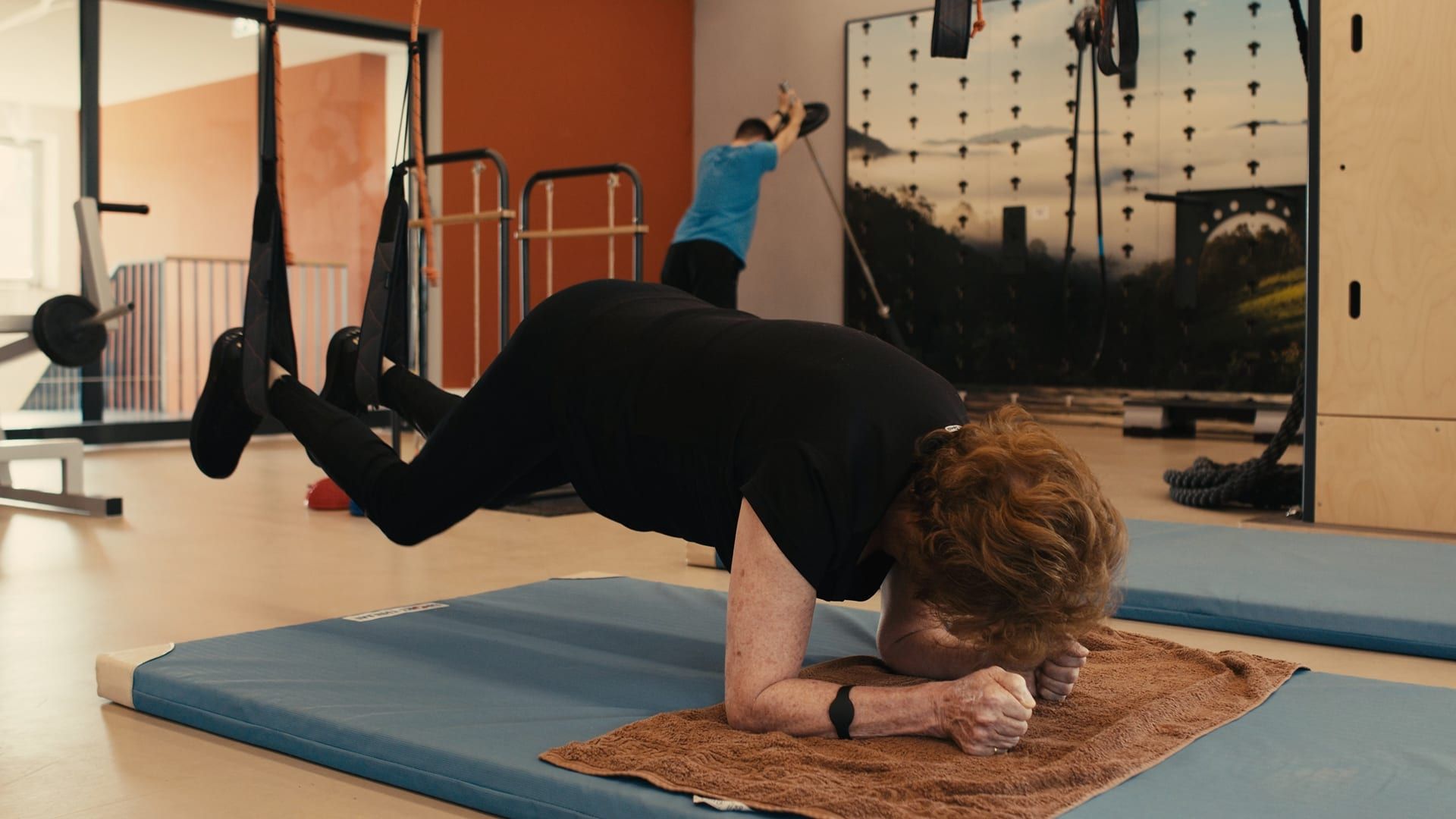 Eine Frau trainiert im Schlingentrainer vor der orangefarbenen Wand des funktionellen Trainingsbereichs.